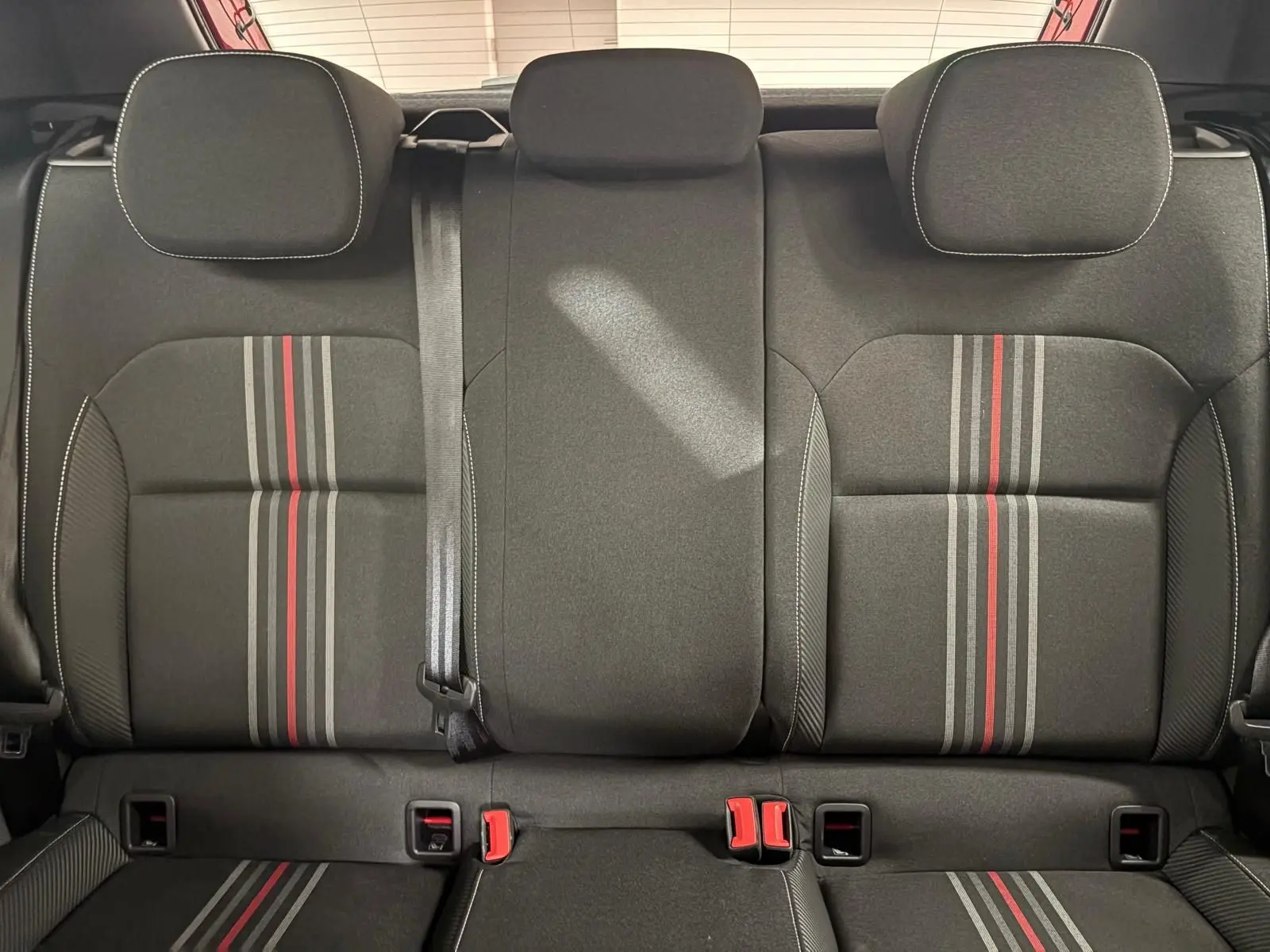 Vue arrière des sièges arrière noirs avec bandes grises et rouges, appuie-têtes et ceinture de sécurité visibles dans une Skoda Fabia.