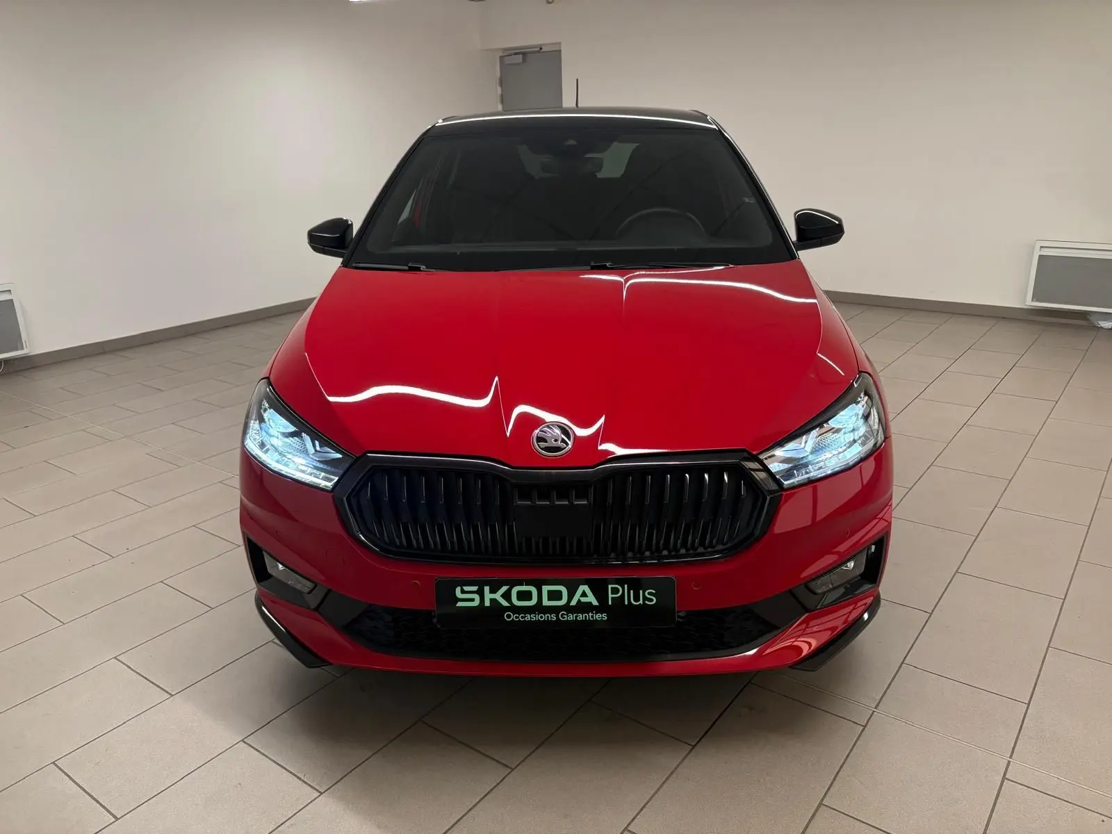 Vue frontale d'une Skoda Fabia 2025 rouge Velvet avec toit noir, phares allumés et calandre noire brillante.