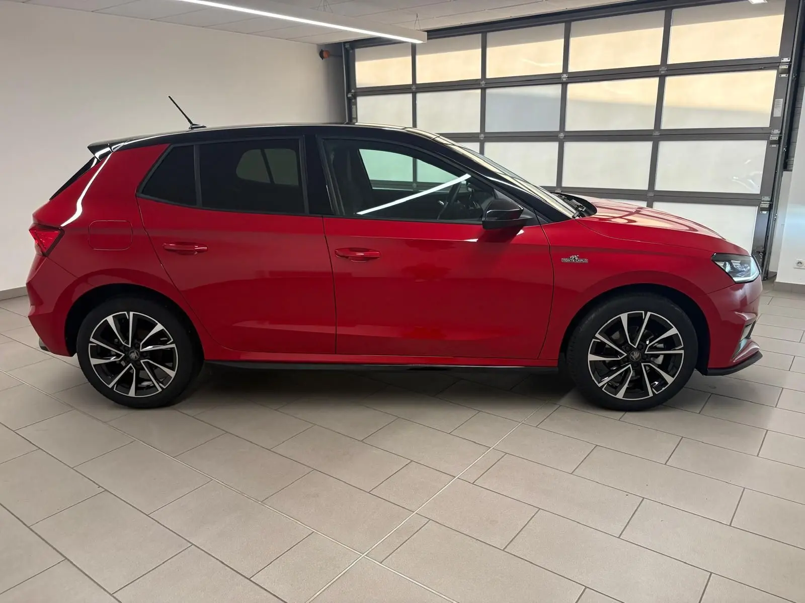 Vue latérale droite d'une Skoda Fabia 2025 rouge Velvet avec toit noir et jantes alliage noires, en intérieur showroom.