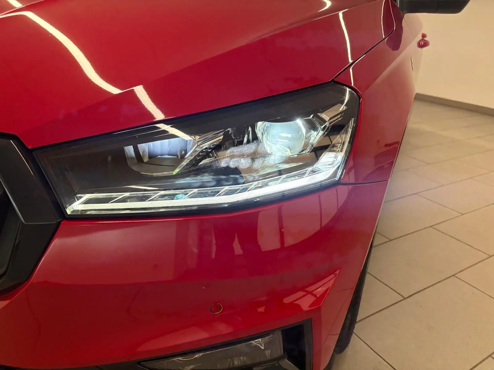 Gros plan sur le phare avant droit d’une Skoda Fabia 2025 rouge Velvet avec toit noir, éclairage LED allumé.