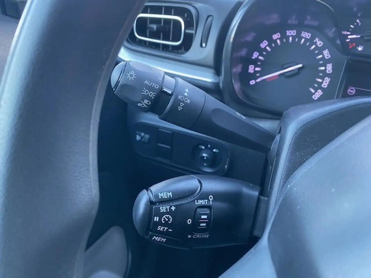 Gros plan sur les commandes au volant de la Citroën C3 Shine 2023, avec tableau de bord et levier de régulateur de vitesse visibles.