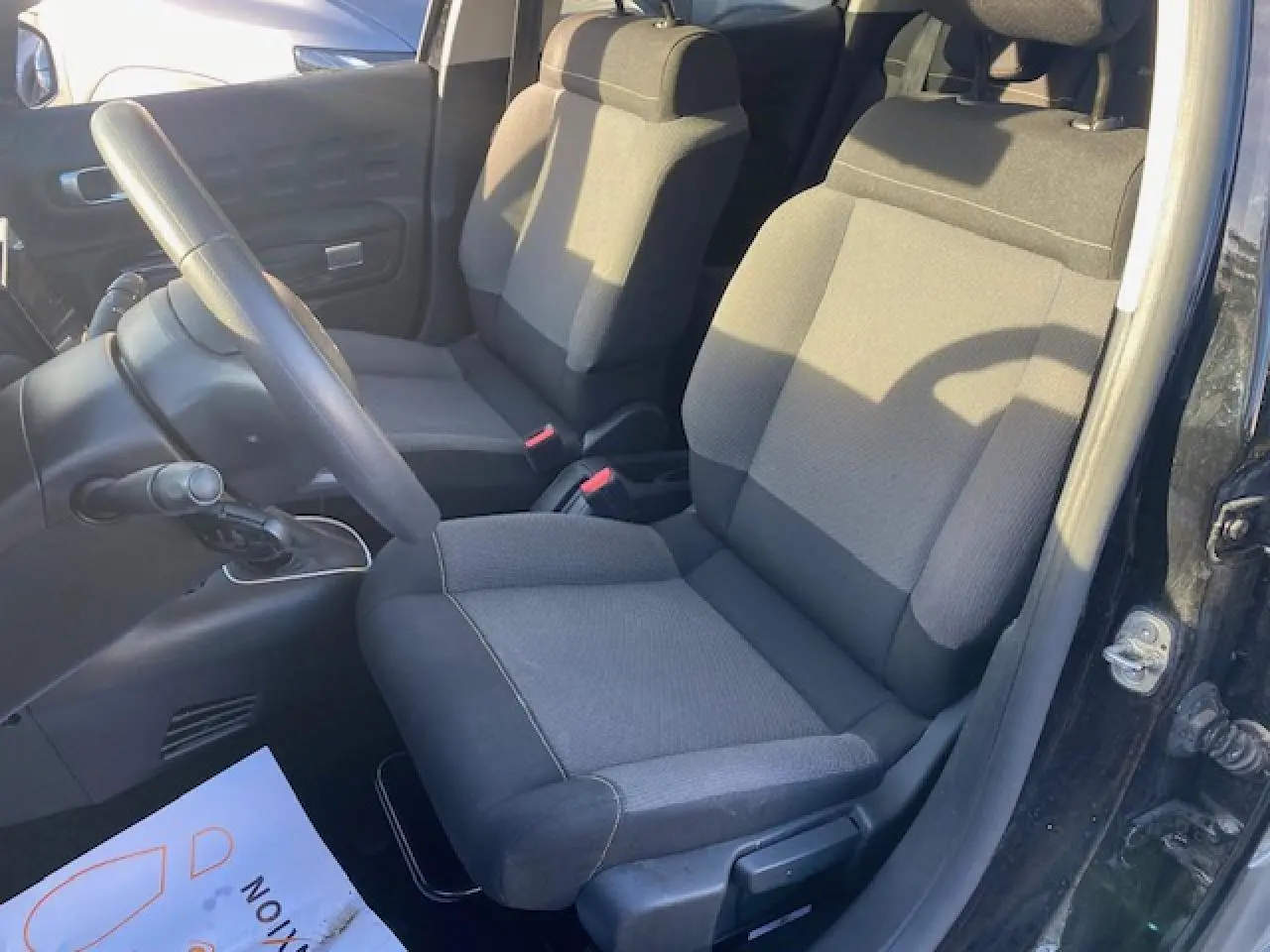 Vue intérieure côté conducteur de la Citroën C3 Shine 2023 avec sièges tissu gris et volant noir.