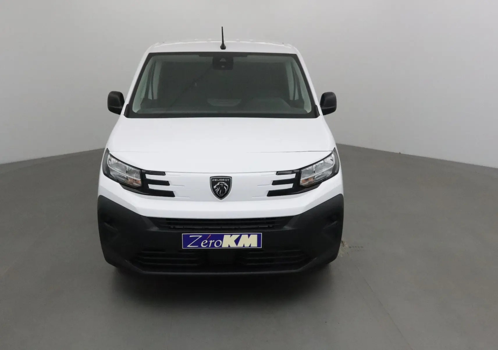Vue frontale d’un Peugeot Partner blanc 2025 avec calandre noire et logo lion central, dans un studio neutre.