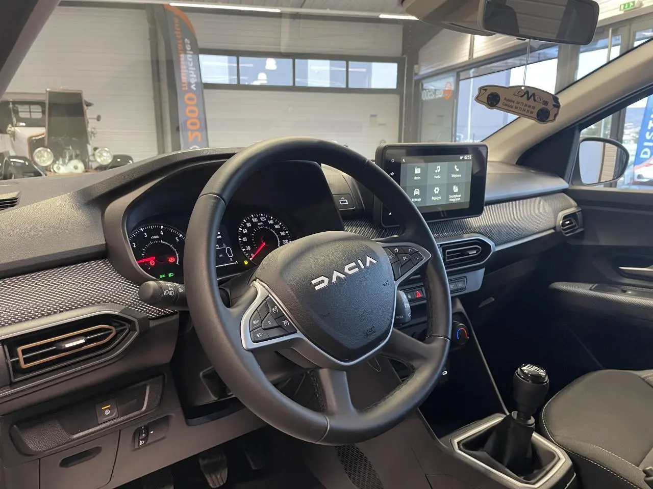 Vue intérieure côté conducteur du tableau de bord et volant Dacia Sandero blanc glacier avec écran tactile et boîte manuelle.