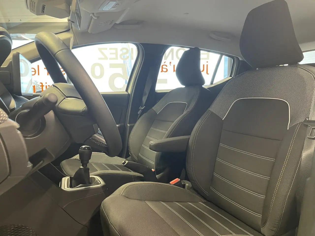 Vue intérieure côté conducteur de la Dacia Sandero Stepway 2025, sièges noirs avec coutures blanches et accoudoir central.