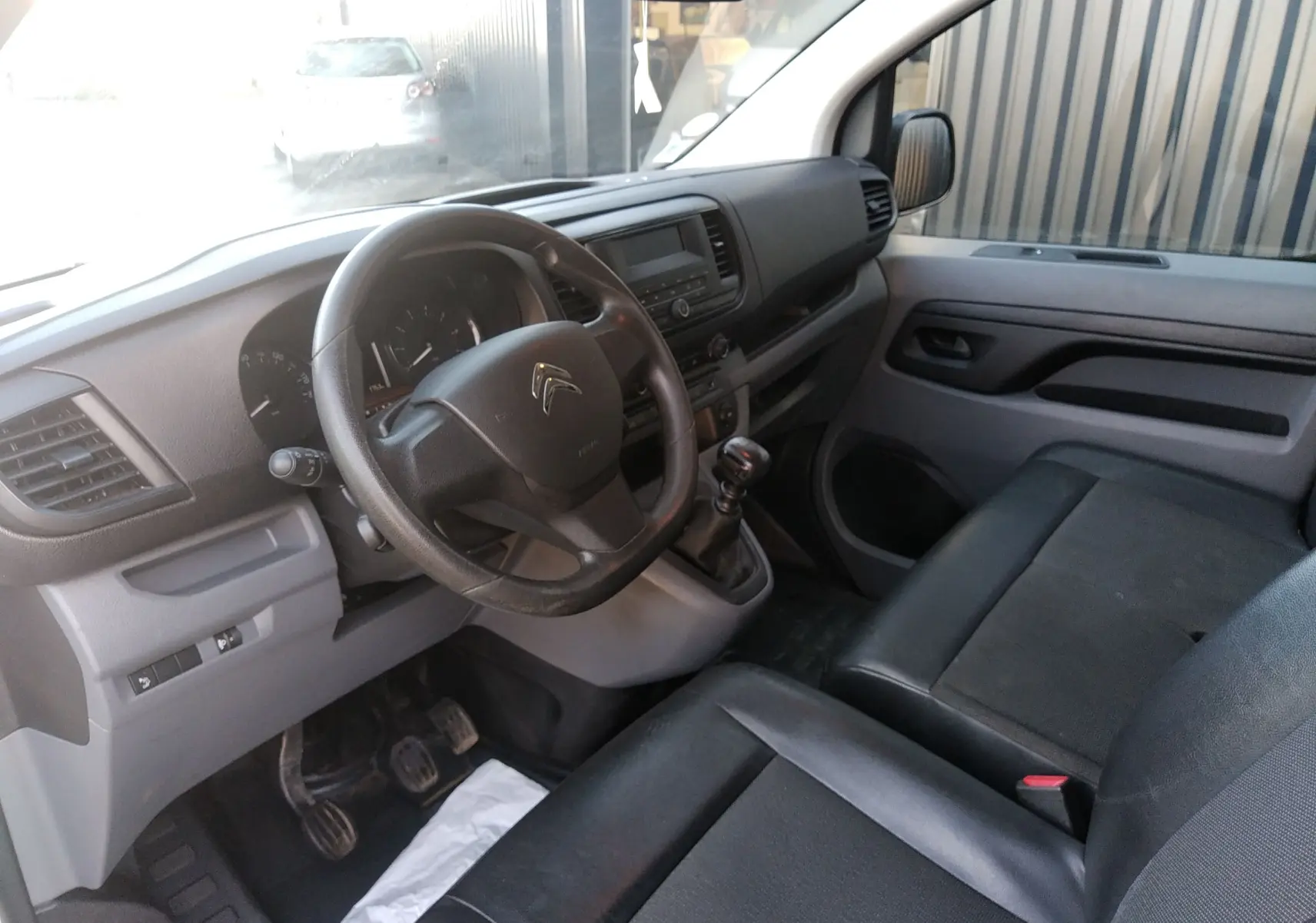 Vue intérieure côté conducteur du Citroën Jumpy blanc 2021, montrant le volant, tableau de bord et sièges noirs.