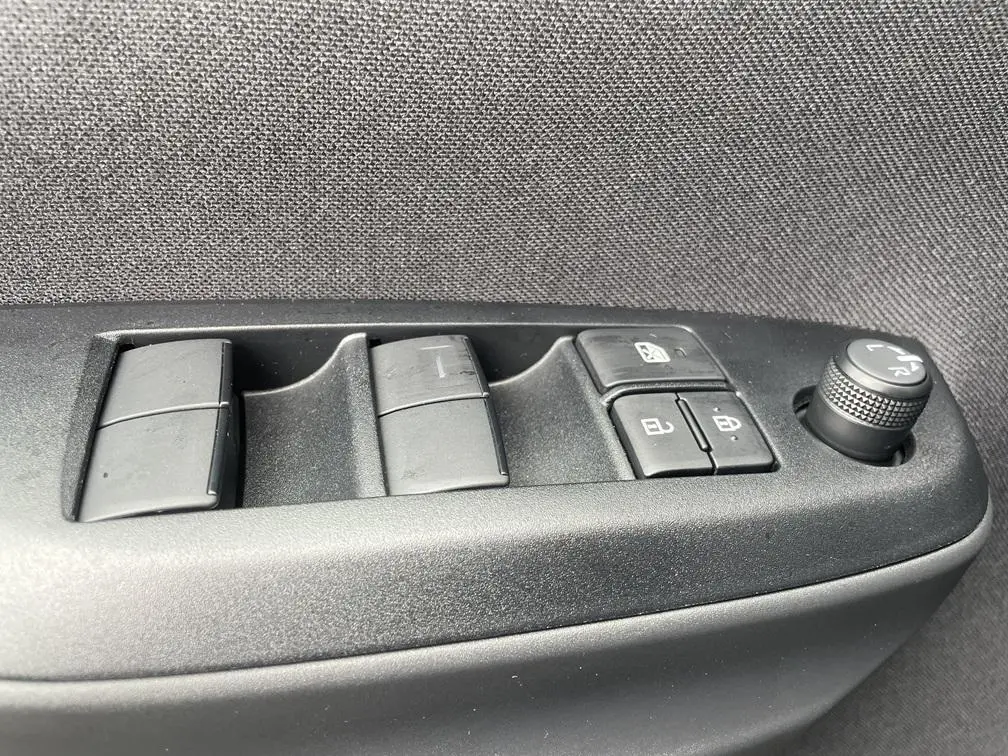 Gros plan sur les commandes de lève-vitres et réglage des rétroviseurs côté conducteur d'une Toyota Yaris Cross gris clair.