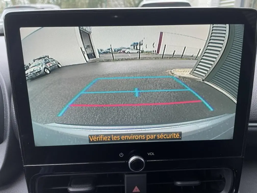 Vue arrière via caméra de recul du Toyota Yaris Cross gris clair, avec lignes de guidage bleues et rouges visibles à l'écran.