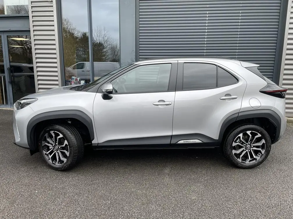 Profil droit d'une Toyota Yaris Cross gris clair avec jantes alliage et protections noires autour des passages de roues.
