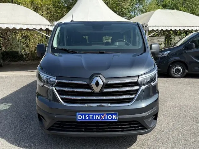 Vue frontale d'un Renault Trafic Combi L2 gris comète, mettant en valeur sa calandre chromée et ses phares LED.
