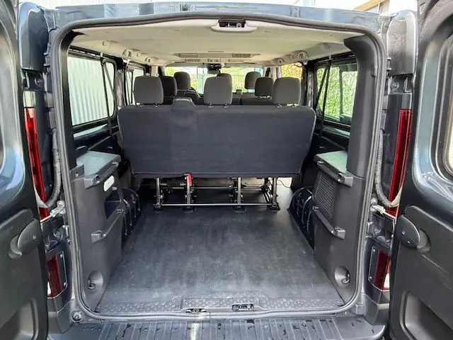 Vue arrière ouverte du Renault Trafic Combi gris comète, montrant l'espace de chargement et la banquette arrière pour 9 places.