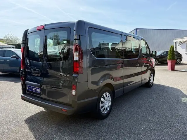 Vue 3/4 arrière droite d'un Renault Trafic Combi gris comète 2022, grand utilitaire 9 places avec vitres latérales teintées.