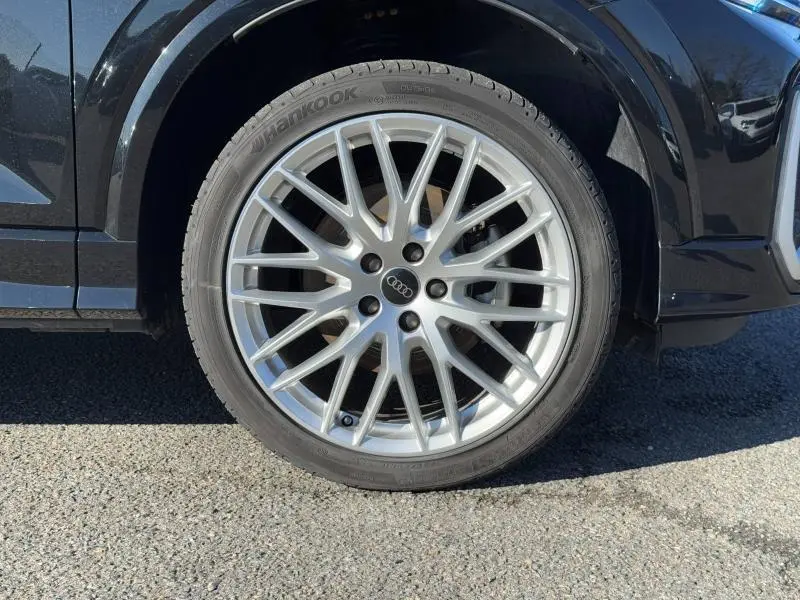 Gros plan sur la roue avant droite de l'Audi Q2 30 TDI S line noire métallisée avec jante alu multibranches argentée.