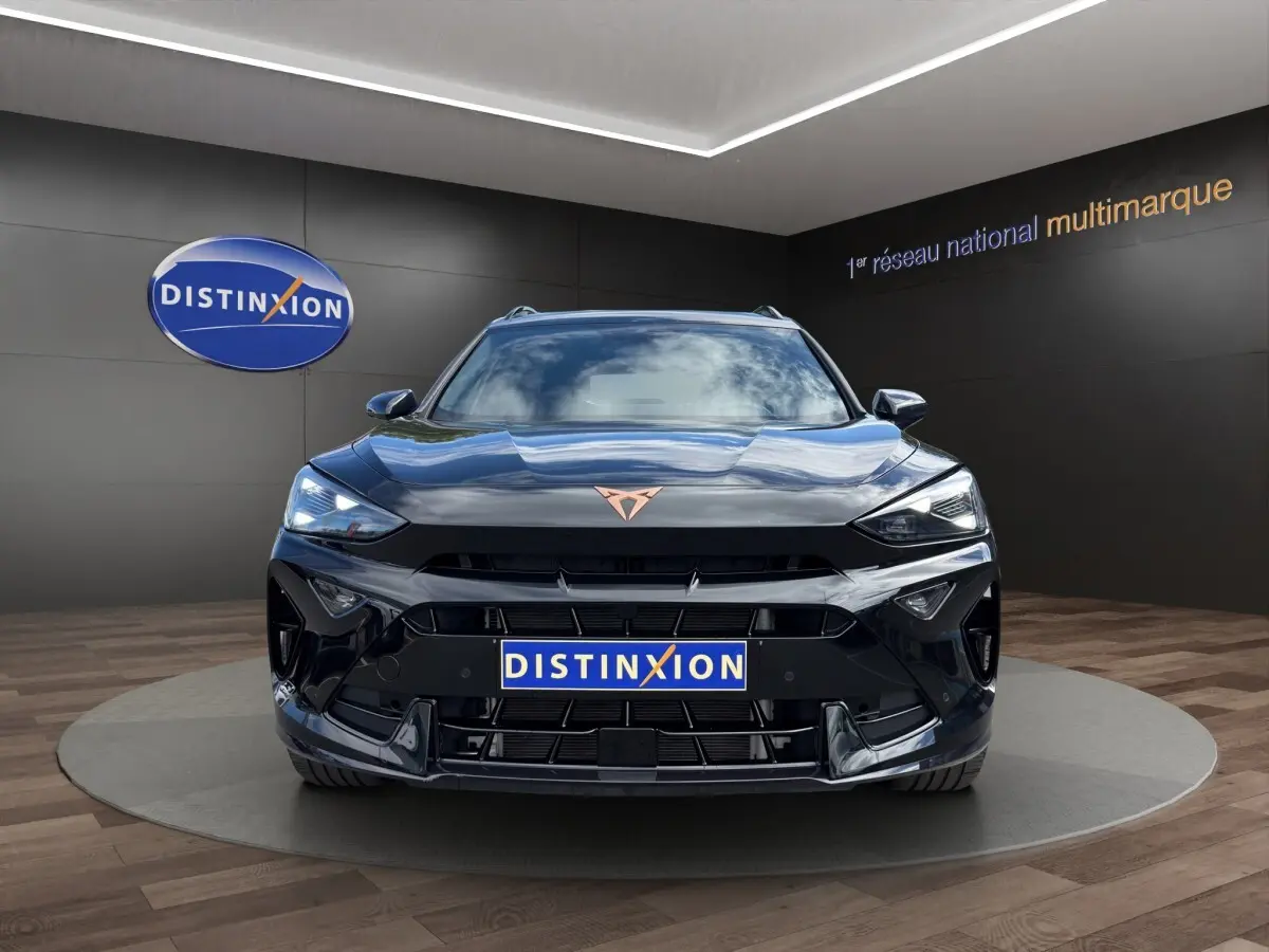 Vue frontale d'un CUPRA Formentor noir brillant avec logo cuivré, dans un showroom au sol bois et mur sombre.