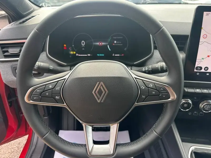 Vue centrée sur le volant multifonction de la Renault Clio Rouge Flamme, avec tableau de bord numérique et écran tactile visible à droite.