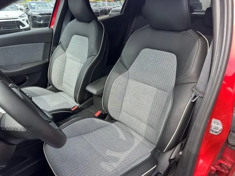 Vue intérieure des sièges avant gris et noir de la Renault Clio Rouge Flamme, avec accoudoir central et porte ouverte côté droit.