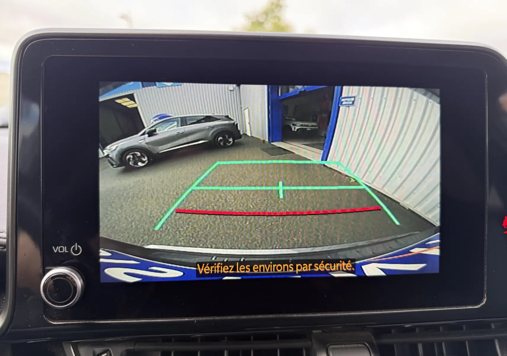 Vue caméra de recul montrant un Toyota C-HR gris atlas garé côté gauche devant un bâtiment industriel.