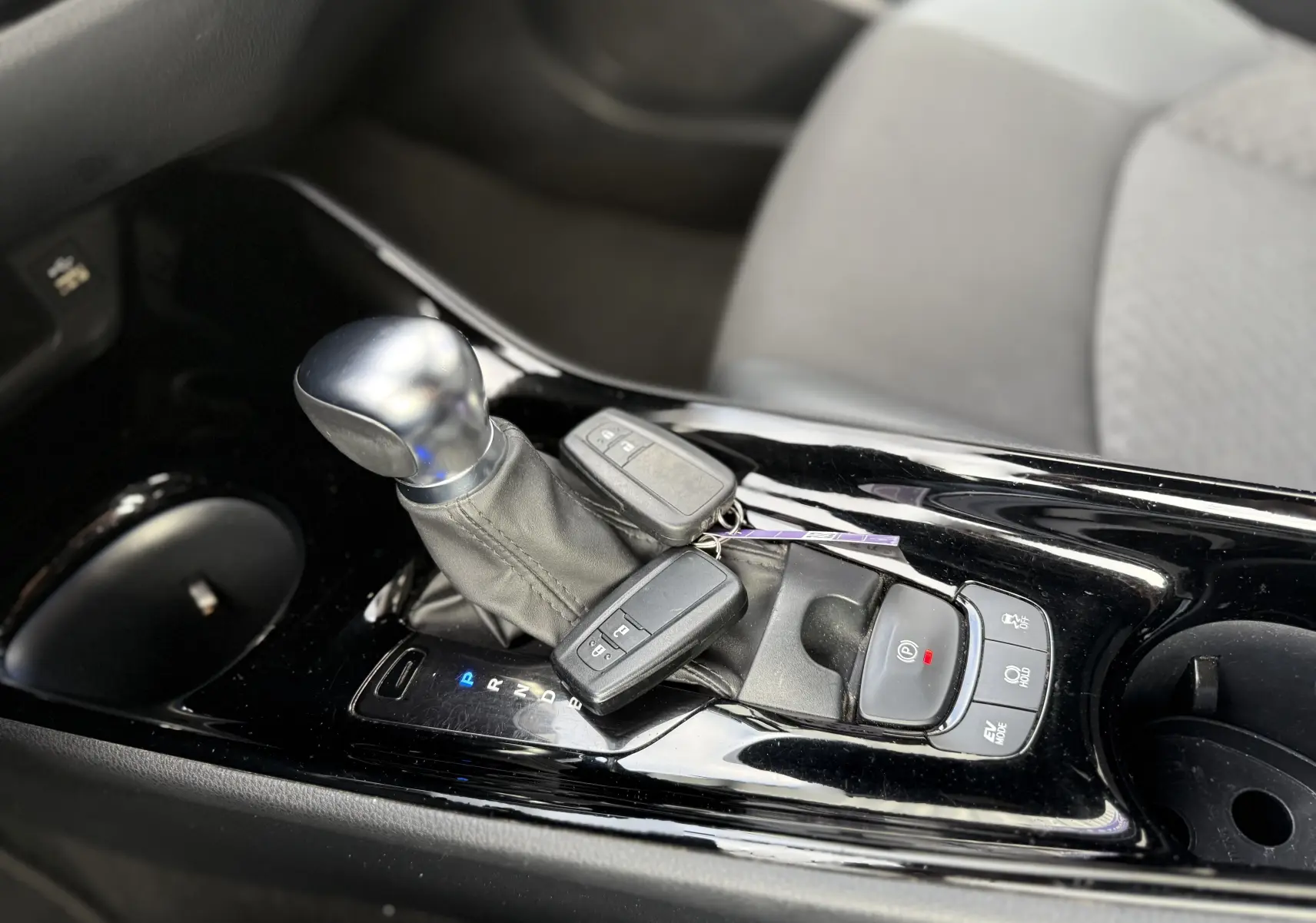 Gros plan sur la console centrale noire brillante du Toyota C-HR 1.8 hybrid avec levier de vitesse et clés posées.