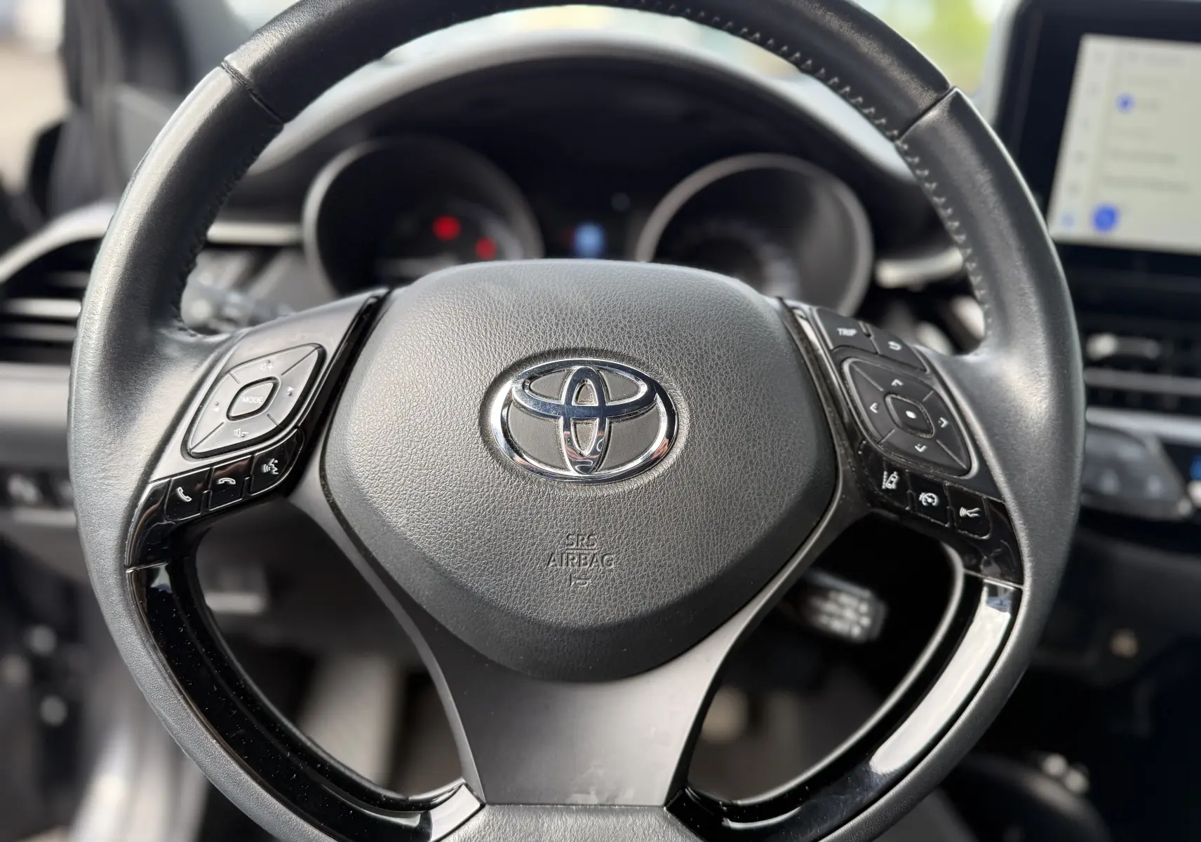 Vue rapprochée du volant noir du Toyota C-HR 1.8 hybrid 2023 avec commandes intégrées et logo central chromé.