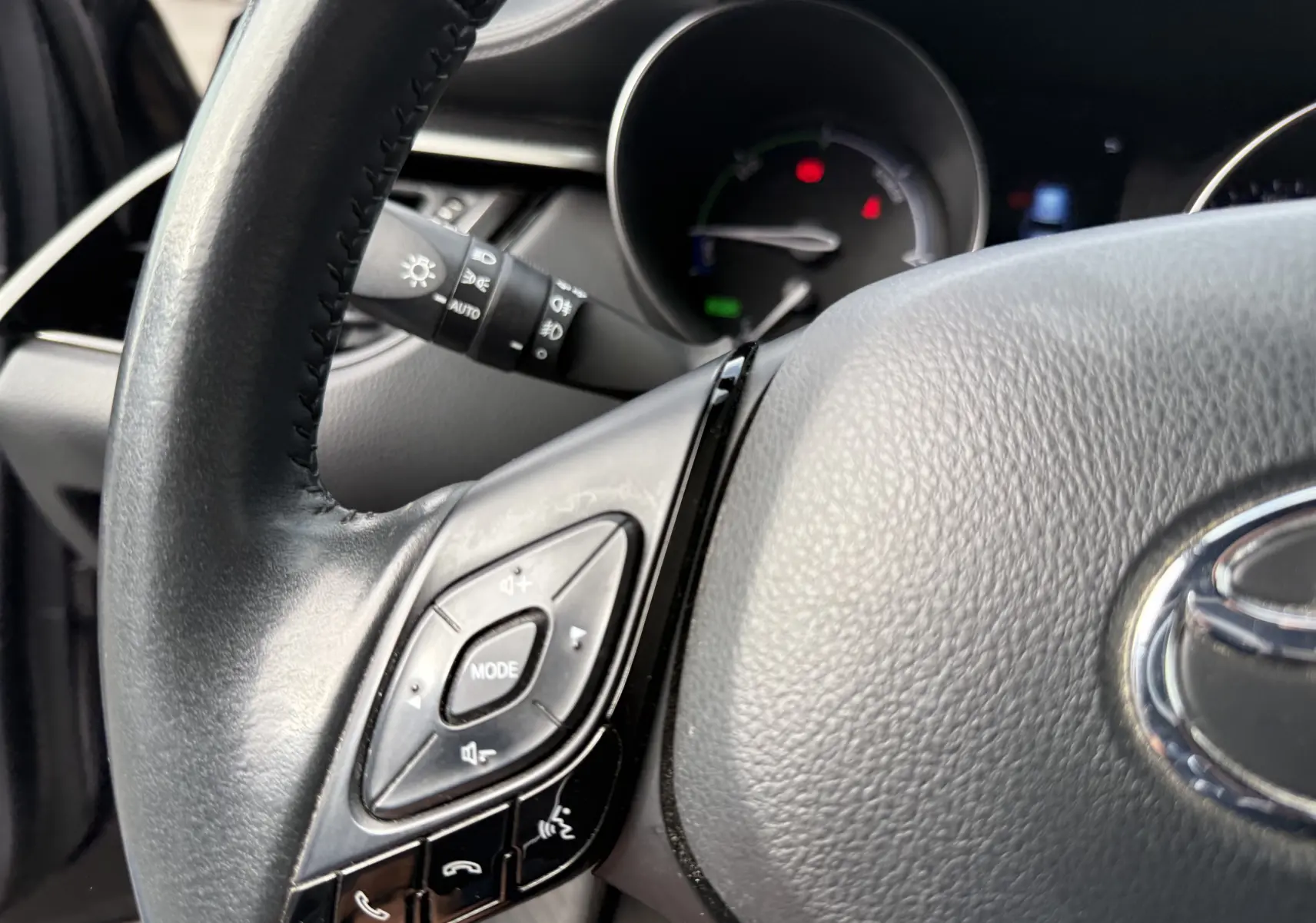 Gros plan sur le volant en cuir noir du Toyota C-HR 1.8 hybrid 2023, avec commandes audio intégrées visibles.