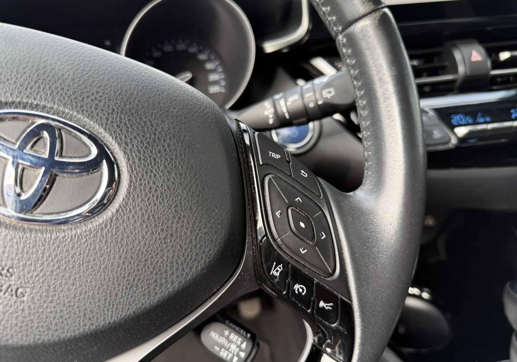Gros plan sur le volant noir du Toyota C-HR 2023, montrant les commandes multifonctions côté droit et le logo Toyota central.