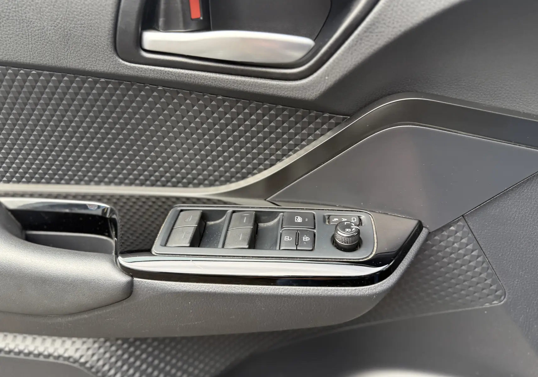 Détail de la porte côté conducteur du Toyota C-HR 1.8 hybrid gris atlas, avec commandes des vitres et réglage des rétroviseurs.