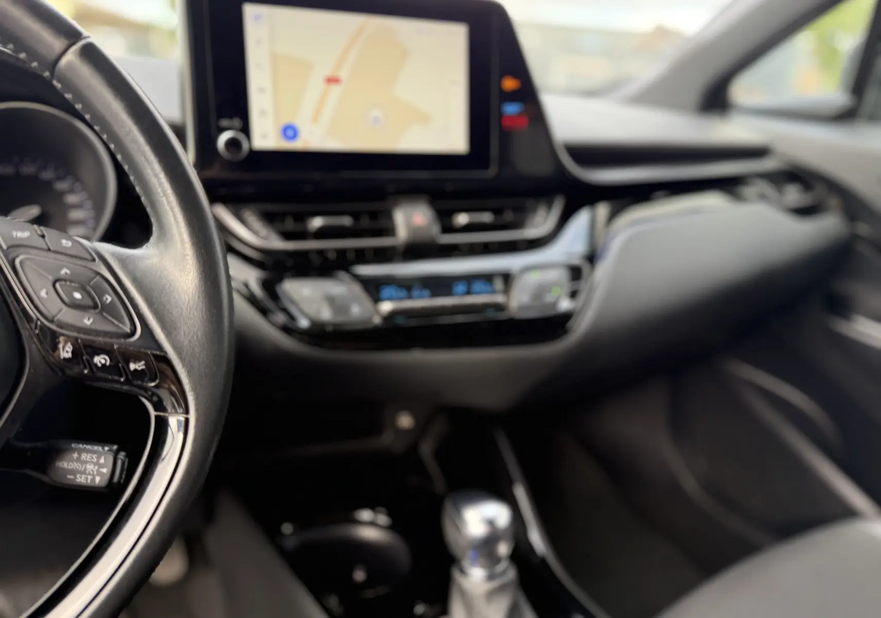 Vue intérieure du tableau de bord et volant côté gauche du Toyota C-HR 1.8 hybrid 2023 avec écran tactile et commandes au volant.