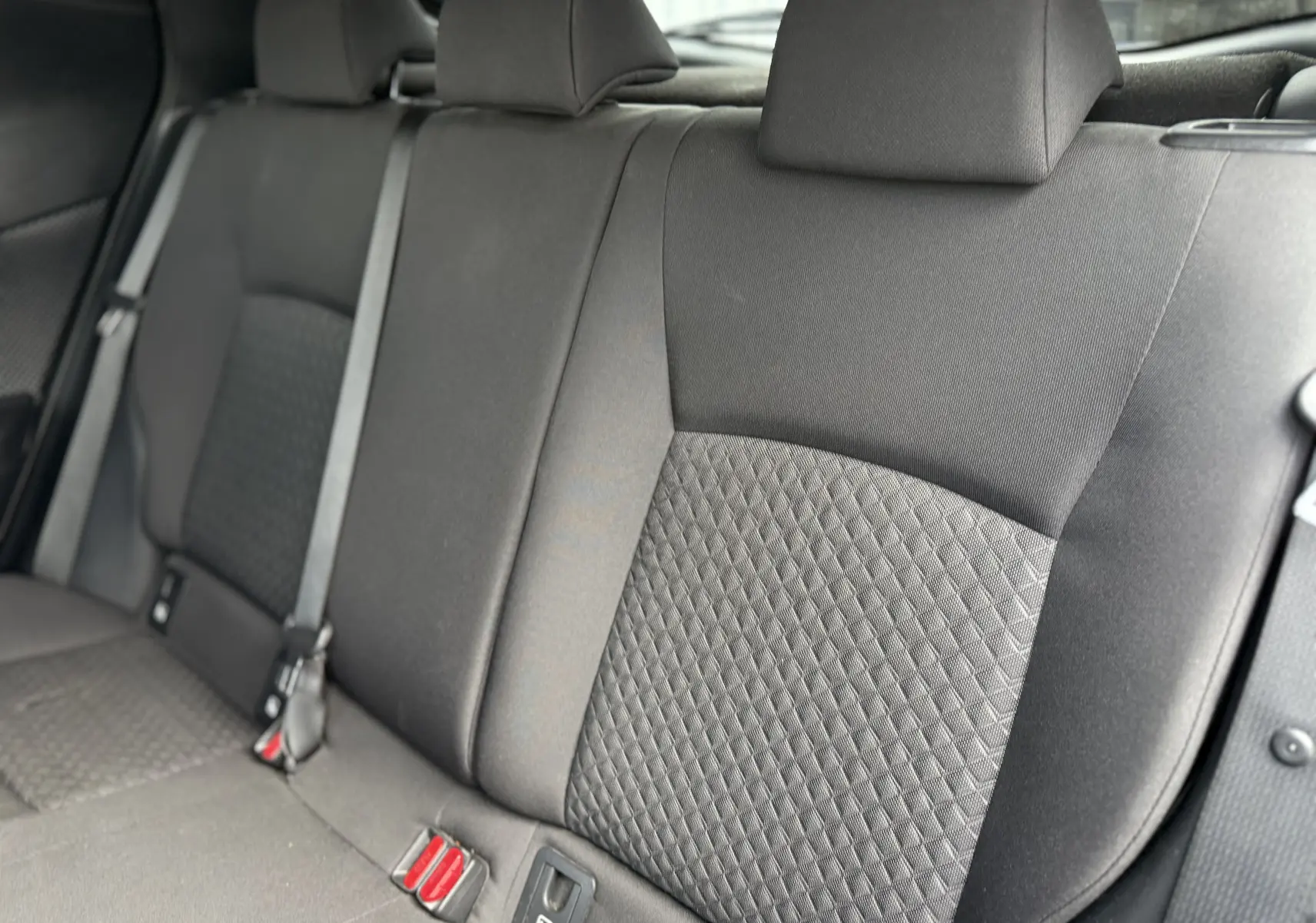 Vue rapprochée des sièges arrière en tissu gris du Toyota C-HR 1.8 hybrid 2023, montrant les ceintures de sécurité.