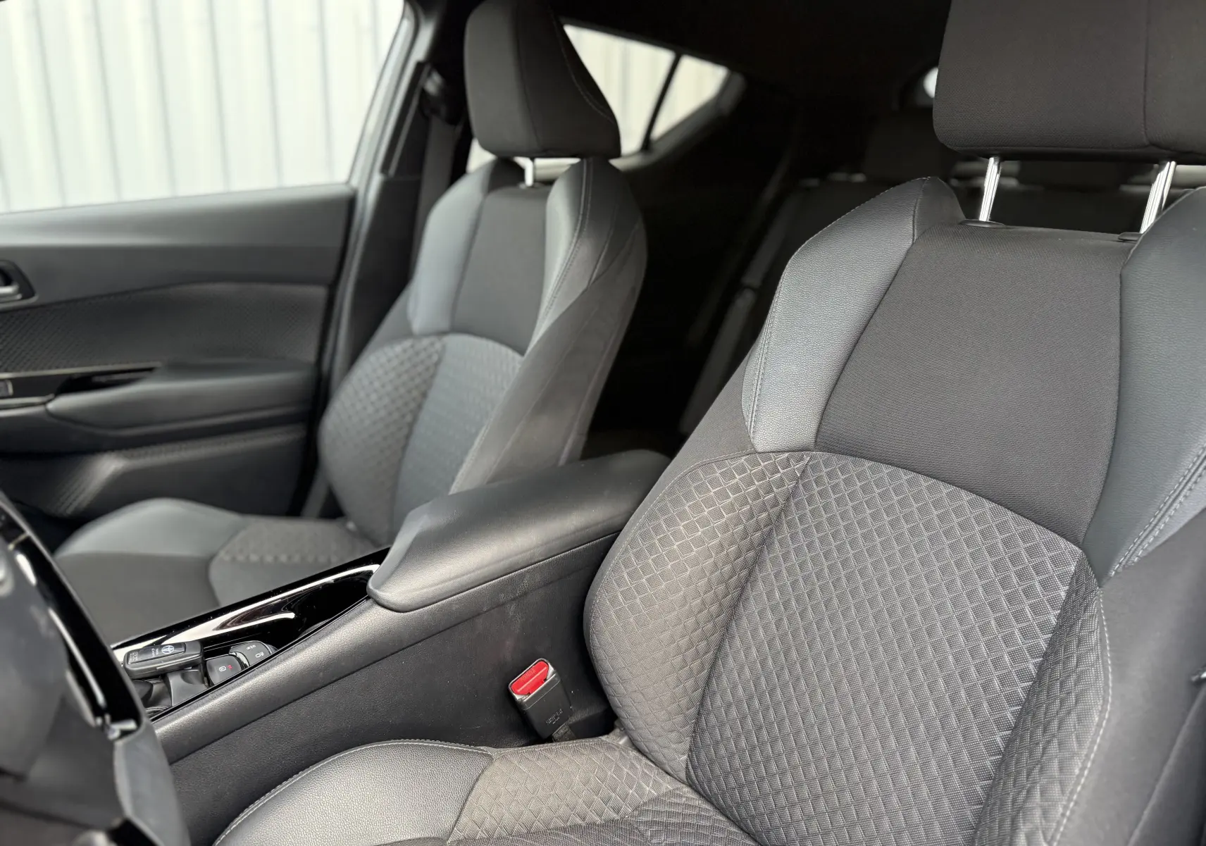 Vue intérieure rapprochée des sièges avant gris tissu du Toyota C-HR 1.8 hybrid 2023 avec accoudoir central noir.