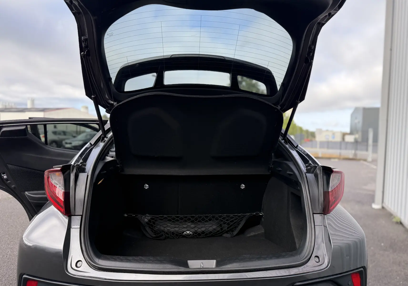 Vue arrière du Toyota C-HR gris atlas 2023 avec coffre ouvert et filet de rangement visible à l'intérieur.