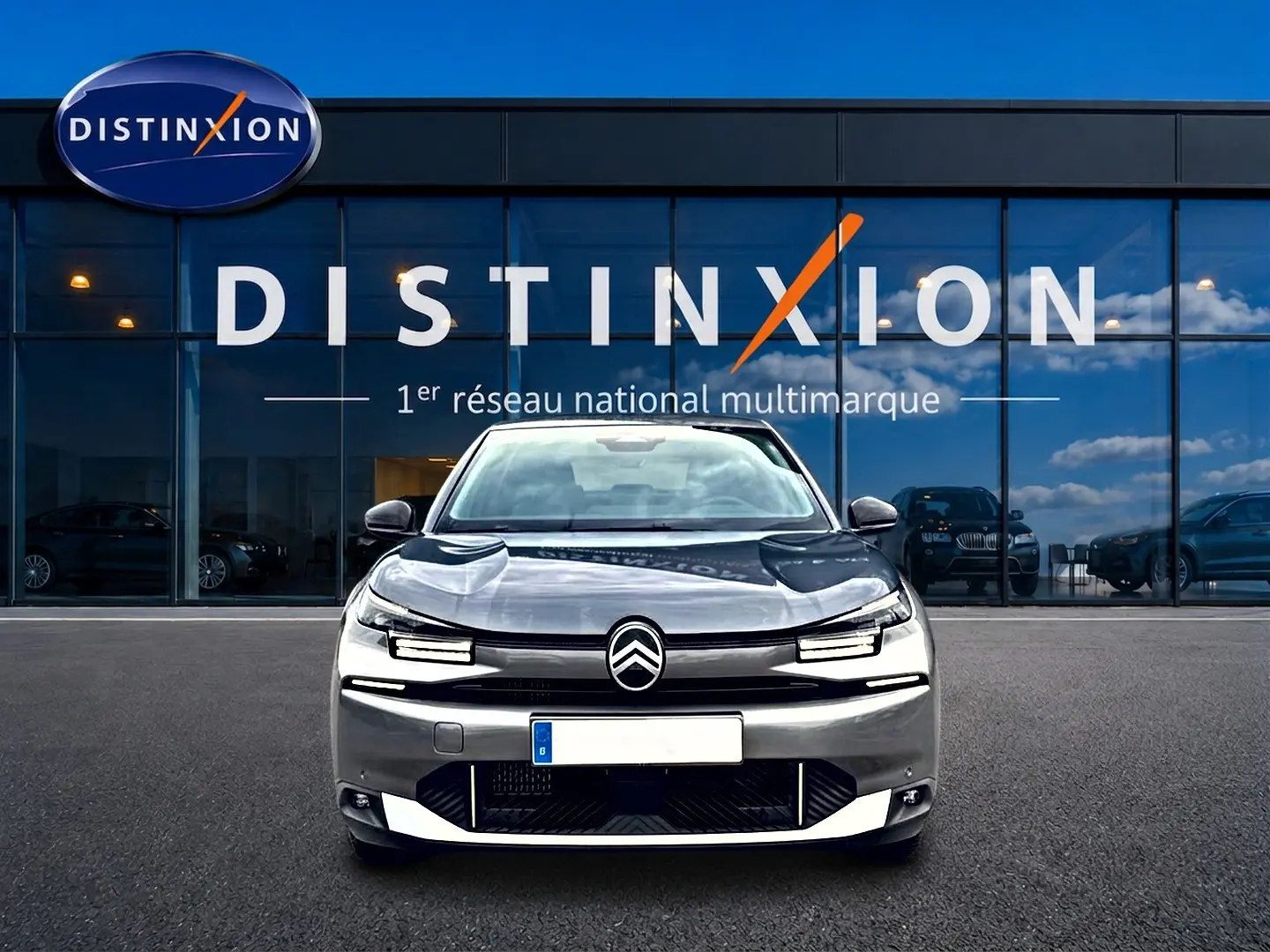 Vue frontale d'une Citroën C4 X gris mercure 2025 avec phares LED et calandre distinctive, devant une vitrine Distinxion.