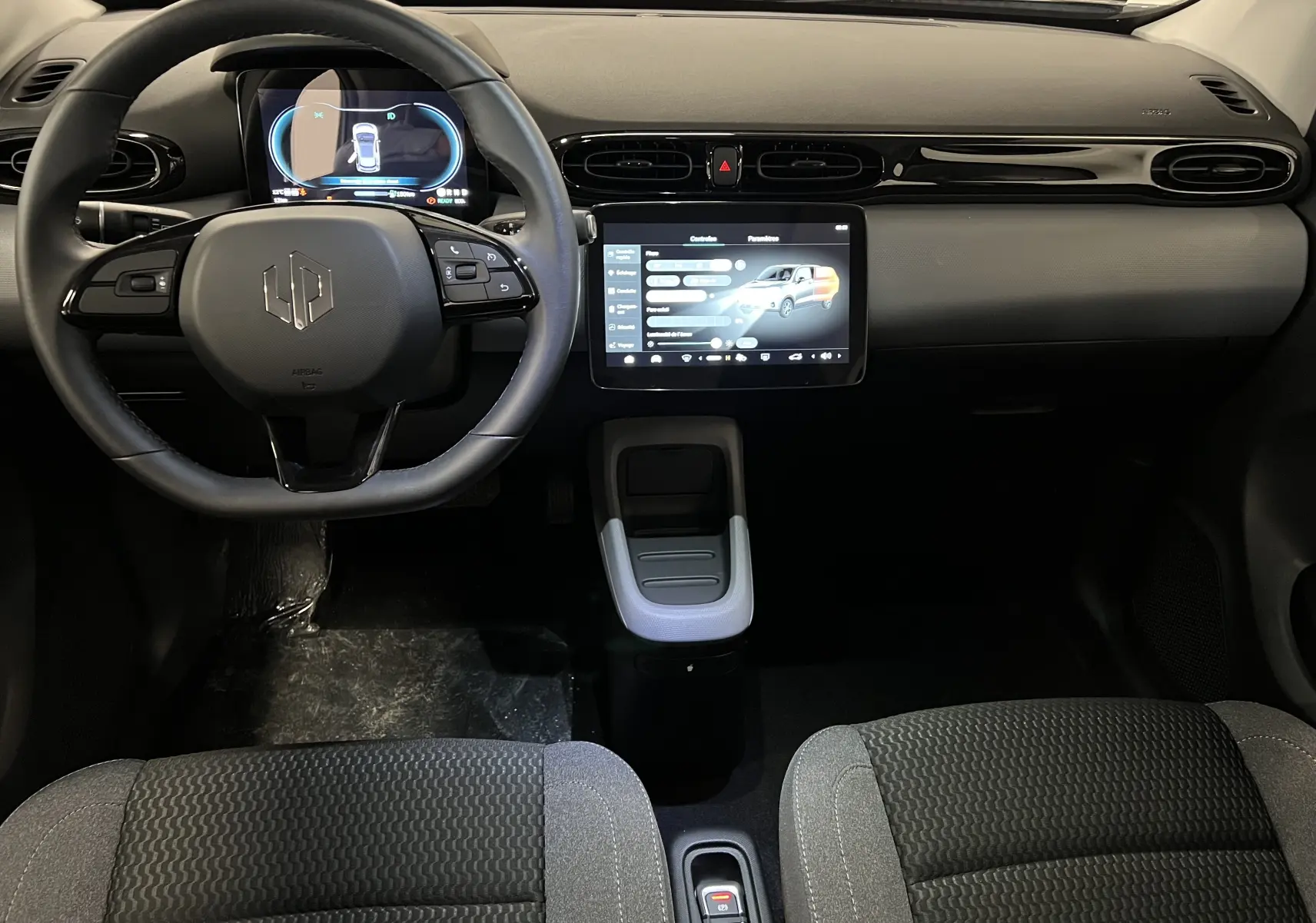 Intérieur du Dacia Spring blanc vu de face, tableau de bord moderne avec écran tactile central et volant multifonction.