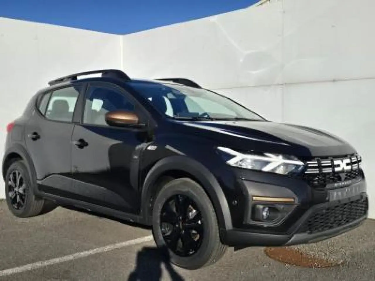 Dacia Sandero III Stepway noir nacré en 3/4 avant droit avec barres de toit et jantes noires distinctives.