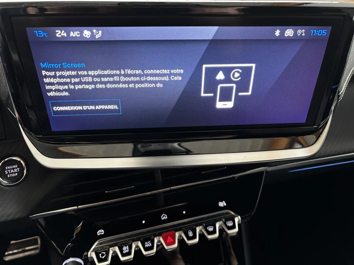 Vue rapprochée de l’écran tactile central et des commandes piano noirs de la Peugeot 208 Hybrid 110 e-DCS6 GT gris clair, avec bouton start visible.