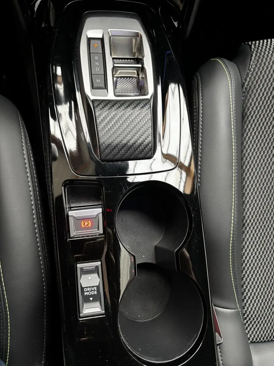 Vue rapprochée de la console centrale noire brillante avec sélecteur de boîte auto et porte-gobelets dans Peugeot 208 Hybrid 110 GT.