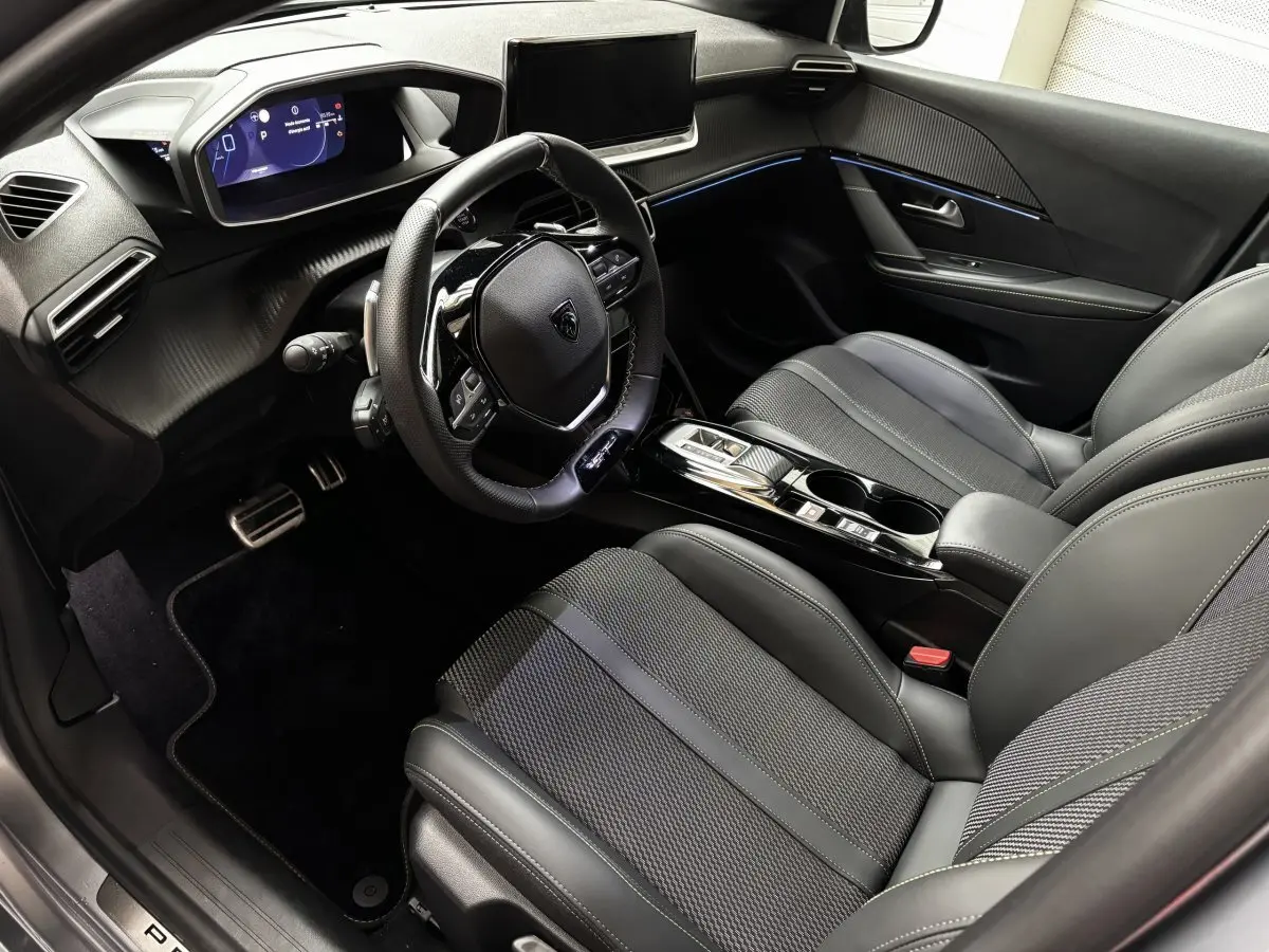 Intérieur avant droit de la Peugeot 208 Hybrid 110 e-DCS6 GT 2025, sièges noirs, volant cuir alu et tableau de bord numérique.