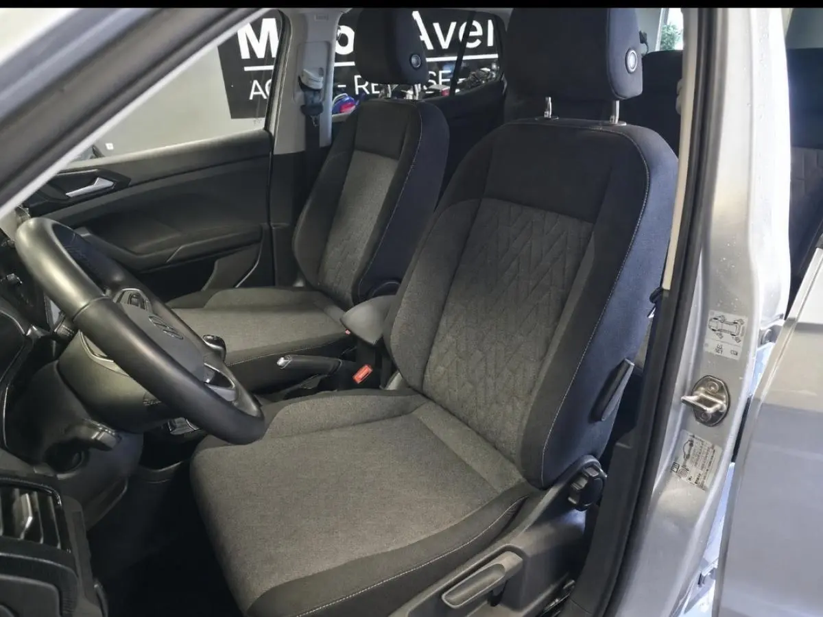 Vue intérieure côté conducteur du Volkswagen T-Cross gris 2025, montrant les sièges en tissu et le volant multifonction en cuir.