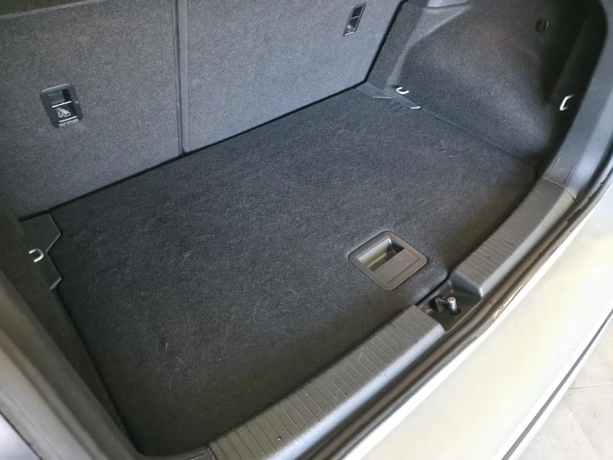 Vue rapprochée du coffre ouvert du Volkswagen T-Cross gris, montrant le tapis de sol et les finitions intérieures.