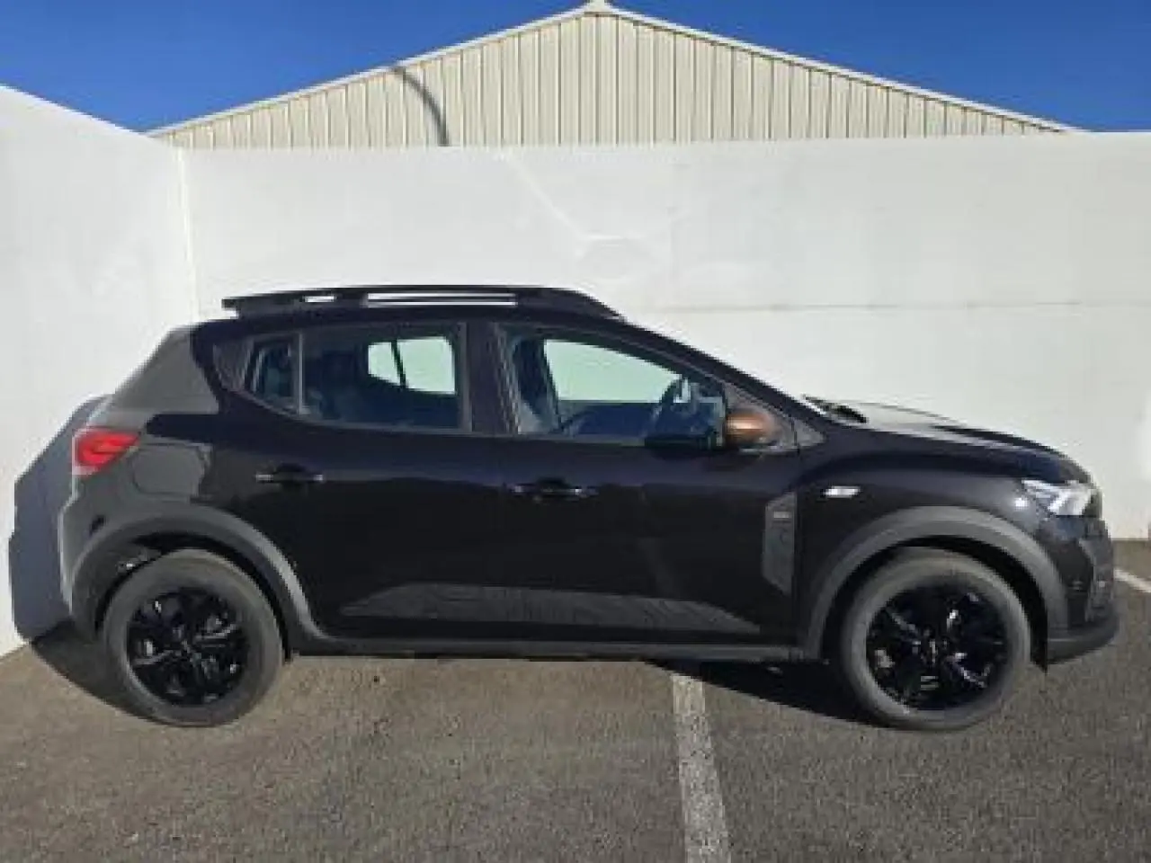 Profil côté gauche de la Dacia Sandero Stepway 2025 noir nacré avec barres de toit et jantes noires brillantes.