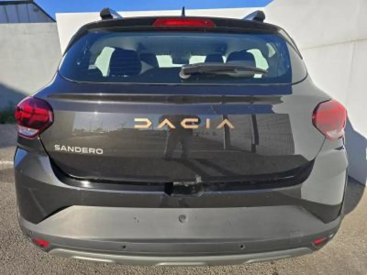Vue arrière d'une Dacia Sandero III Stepway noire nacrée avec logo doré et feux rouges visibles.