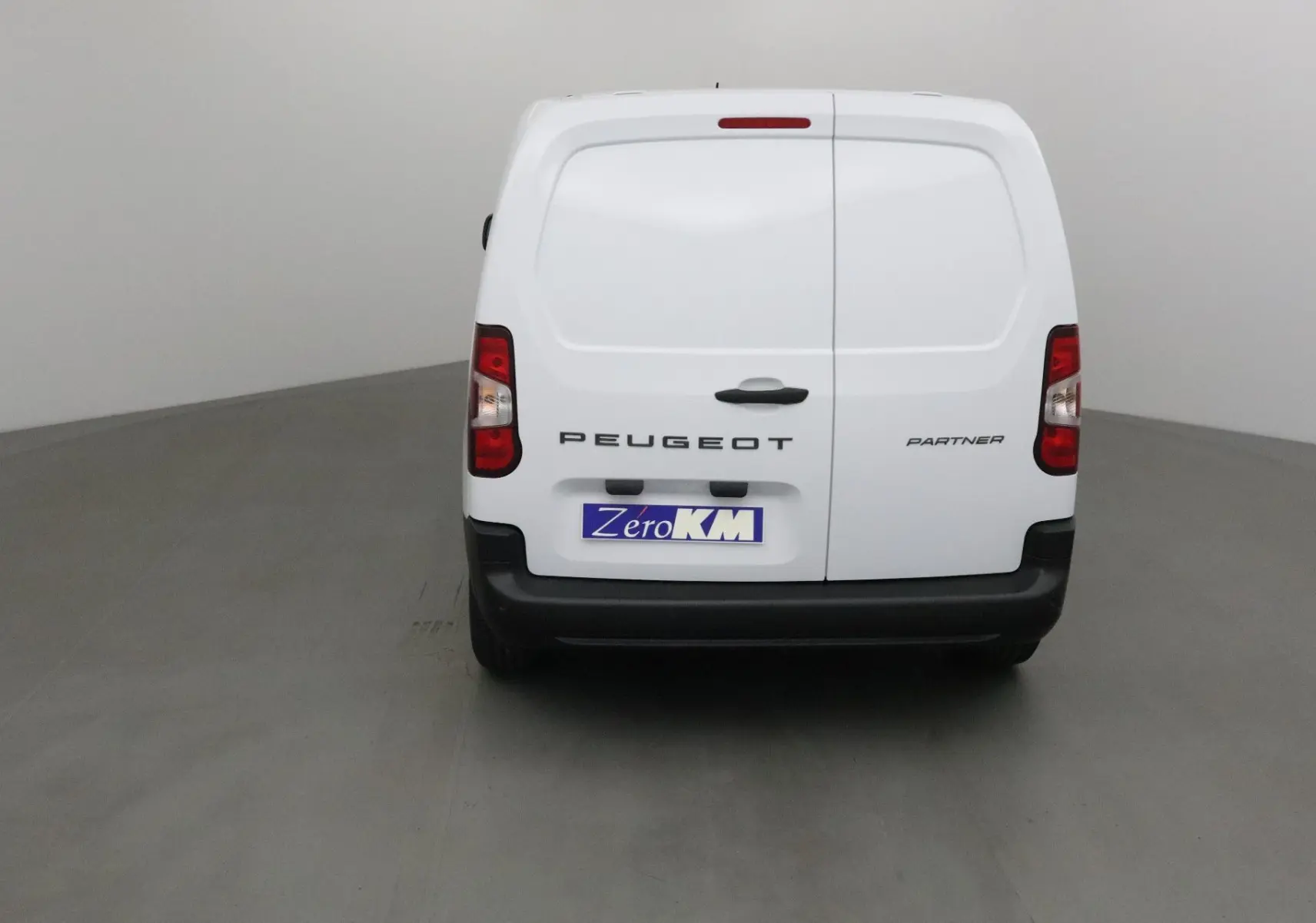 Vue arrière d'un utilitaire blanc Peugeot Partner 2025 avec portes battantes et logo visible.