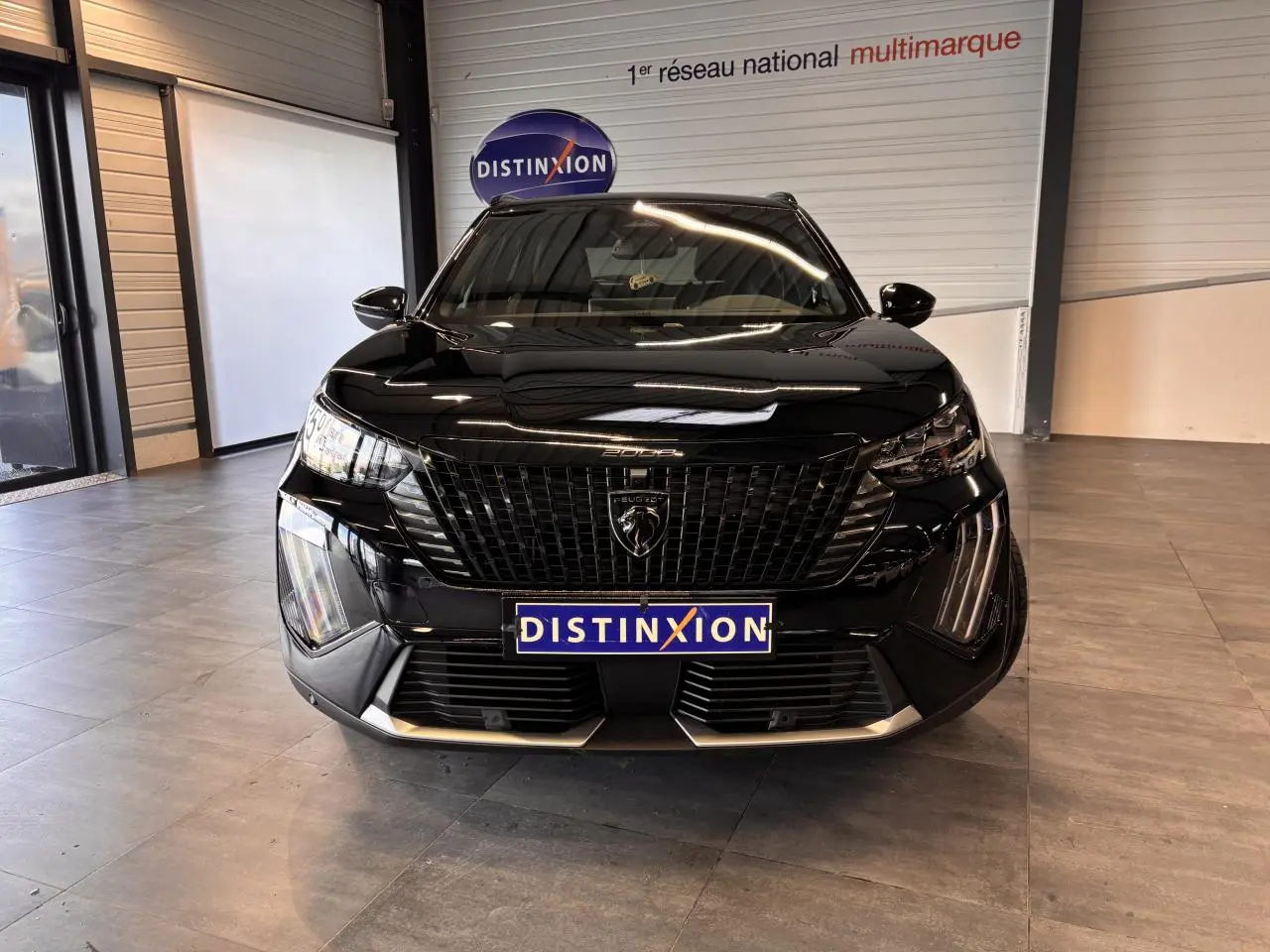Vue frontale d’un Peugeot 2008 noir brillant avec calandre noire et feux LED en showroom.