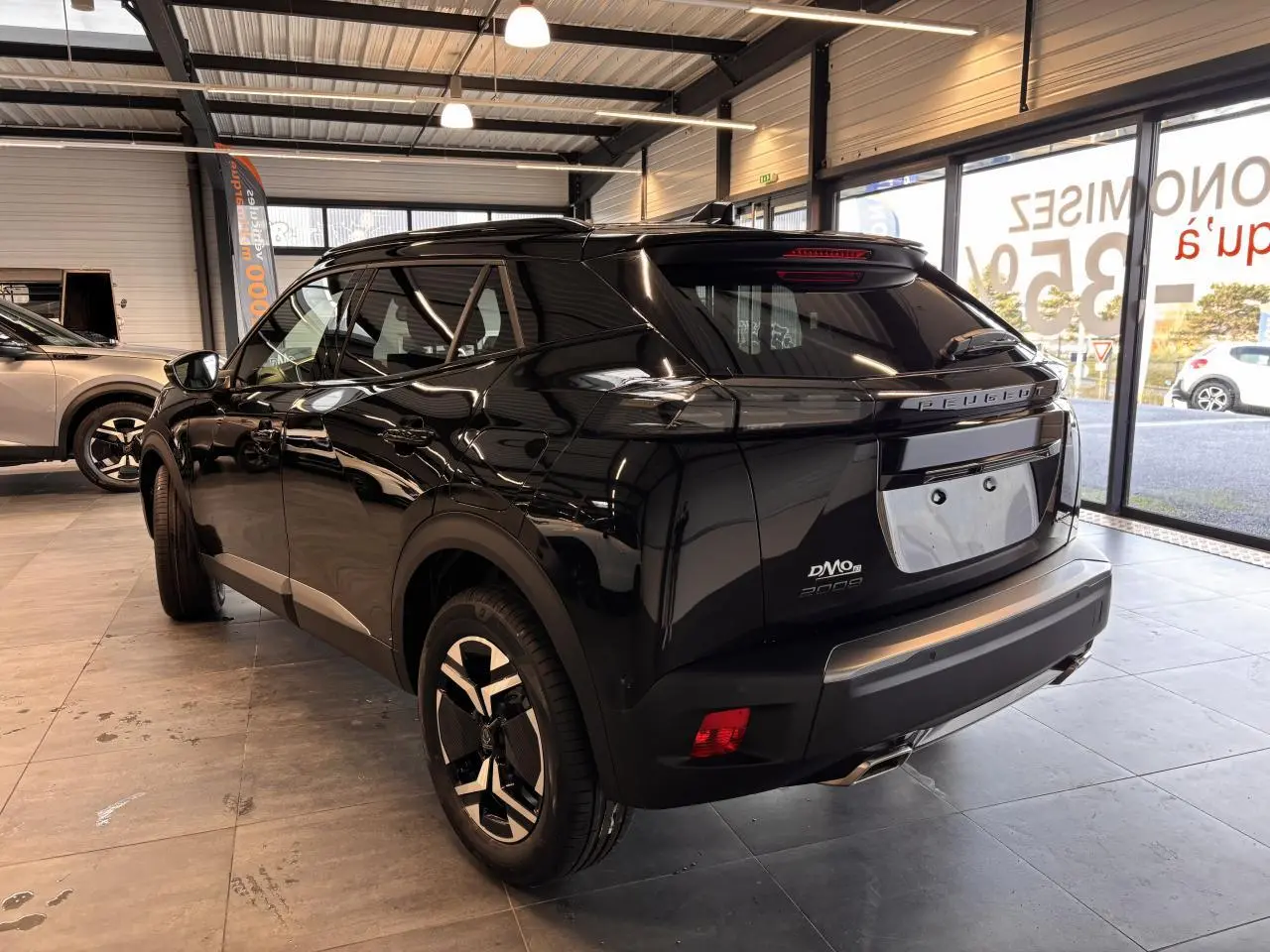 Vue 3/4 arrière droite d'un Peugeot 2008 noir brillant en showroom avec jantes alliage bi-ton et feux arrière LED griffés.