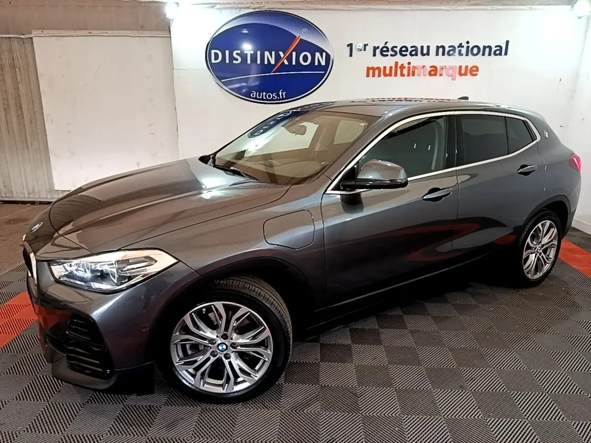 BMW X2 hybride rechargeable gris foncé vue 3/4 avant droit, jantes alliage et prises de recharge visibles