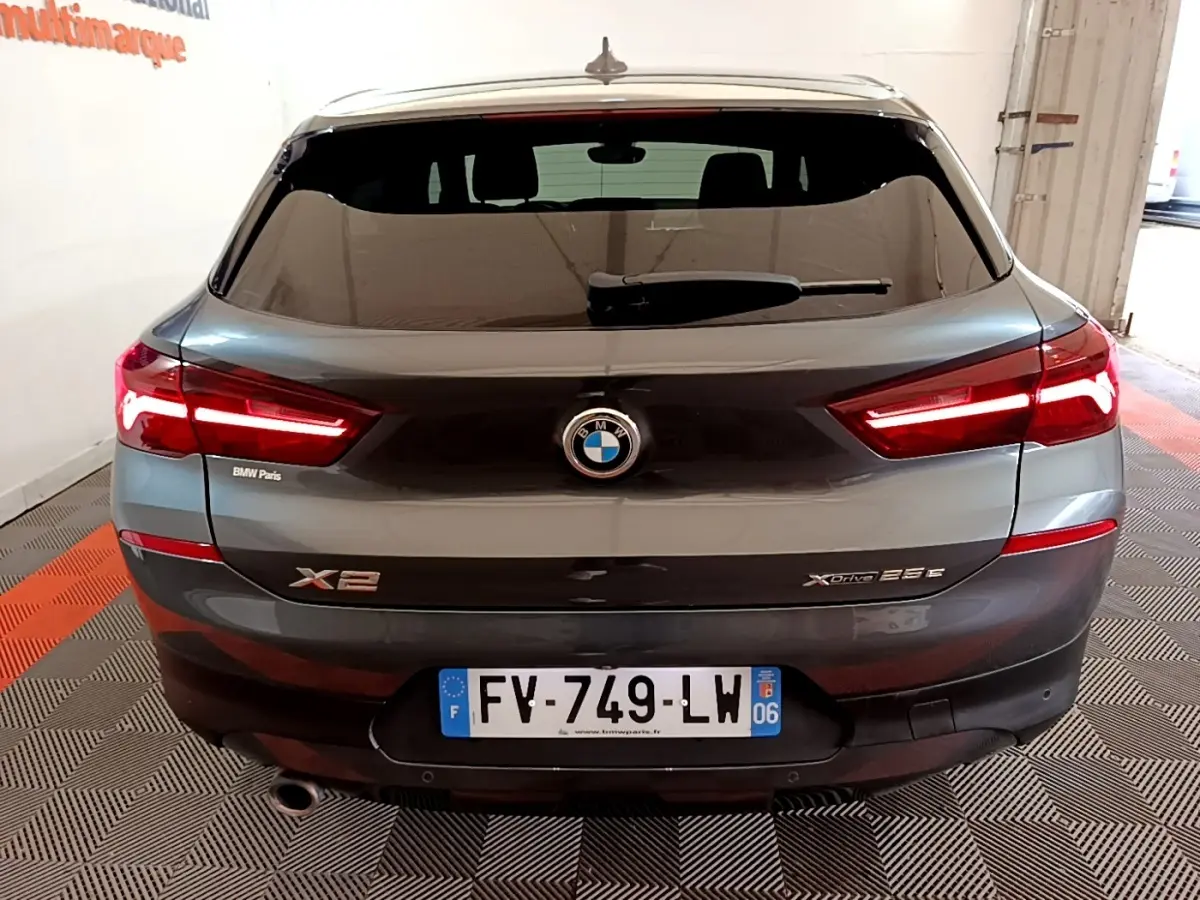 Vue arrière d’une BMW X2 xDrive25e gris foncé avec feux LED allumés dans un garage.