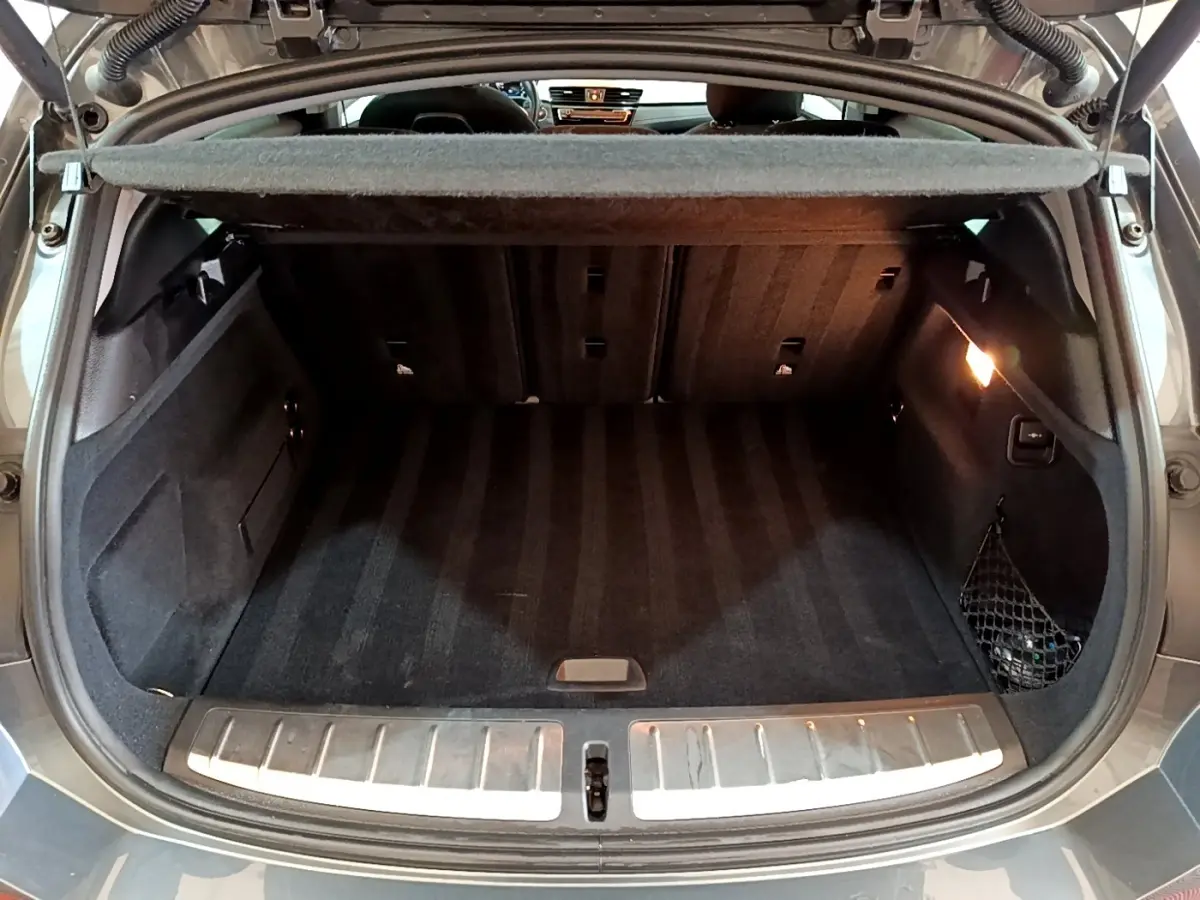 Coffre ouvert noir du BMW X2 xDrive25e vu de l'arrière, avec éclairage intérieur et filet de rangement latéral.