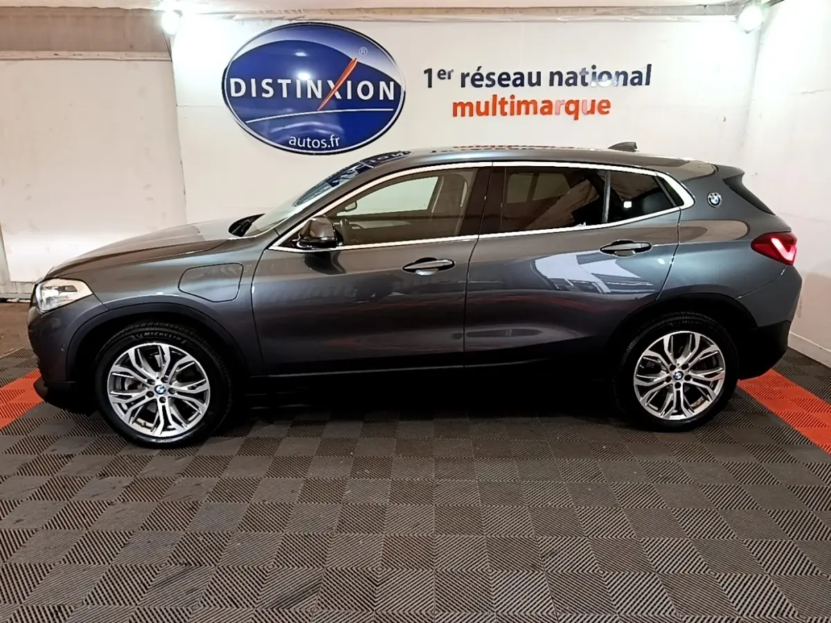 Profil droit d’un BMW X2 xDrive25e gris métallisé hybride rechargeable, avec jantes alliage et logo BMW sur l’aile arrière.