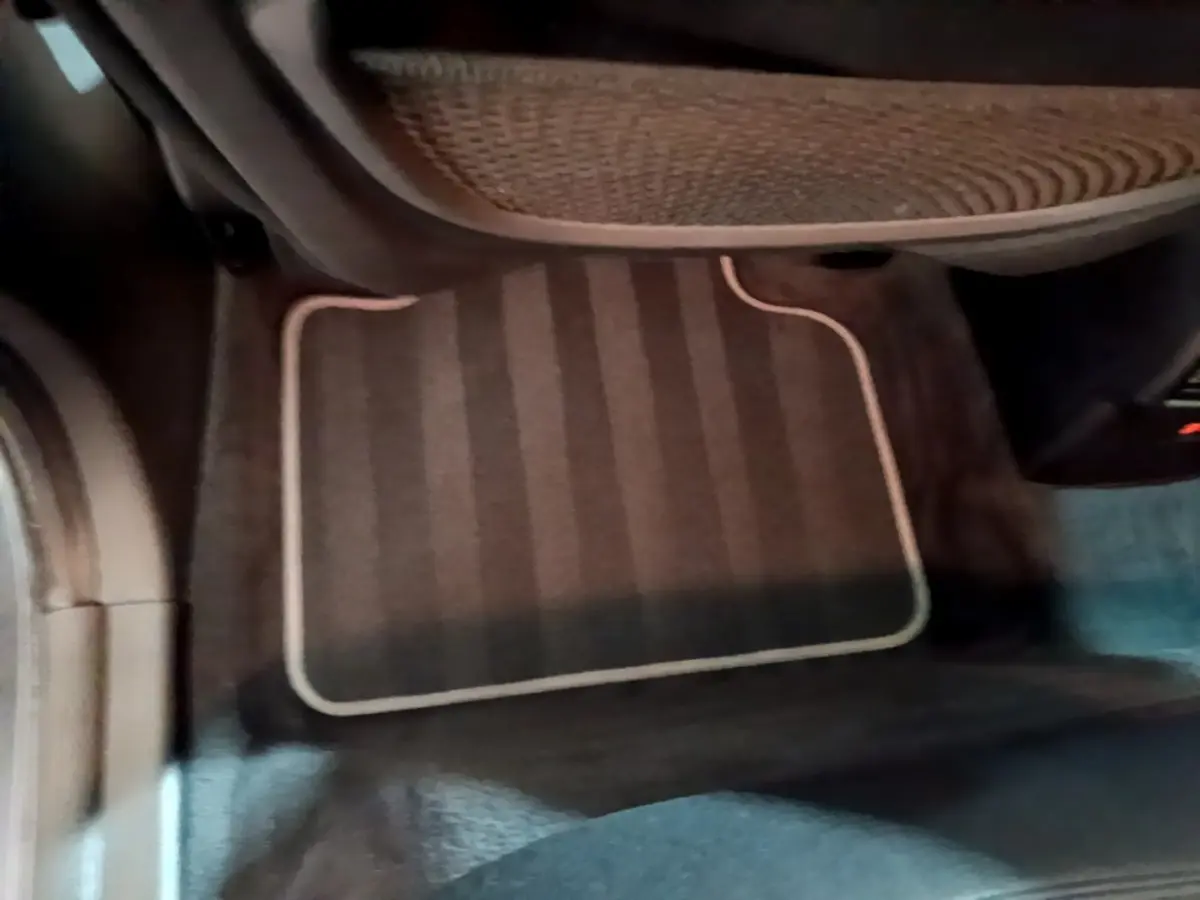 Vue intérieure du tapis de sol côté passager avant d'une BMW X2 hybride rechargeable, couleur sombre avec surpiqûres claires.