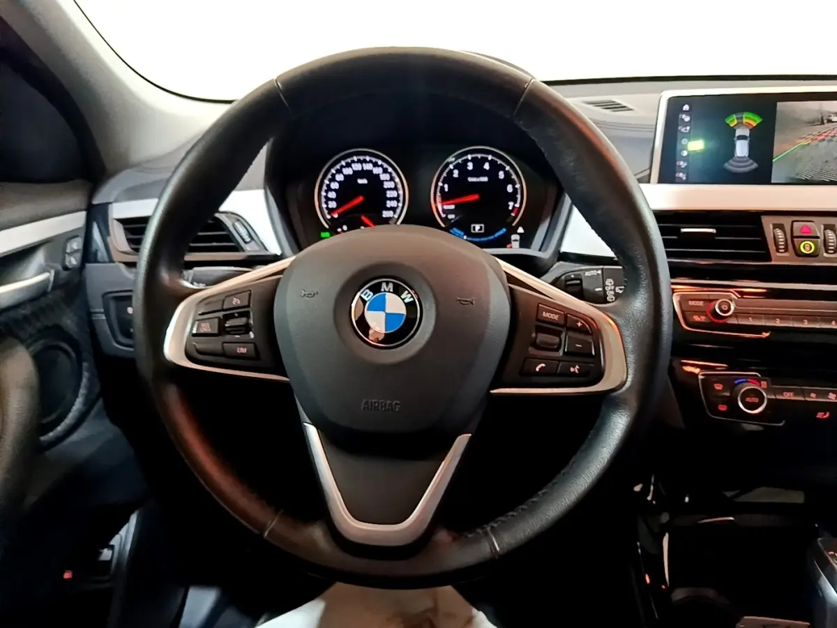 Vue intérieure centrée sur le volant cuir noir de la BMW X2 avec tableau de bord et écran tactile en arrière-plan.