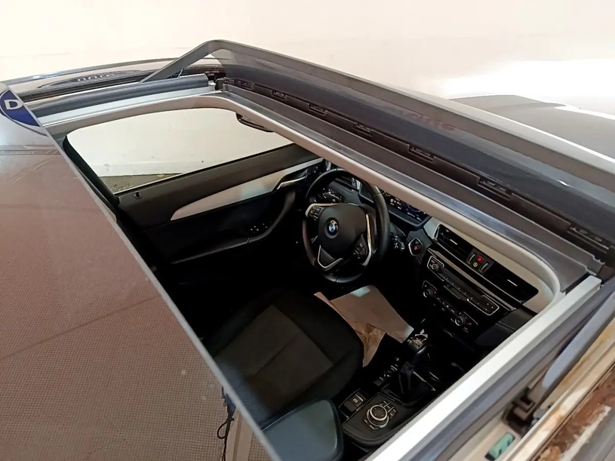 Vue intérieure plongeante du poste de conduite BMW X2 xDrive25e avec toit ouvrant et volant cuir multifonctions.